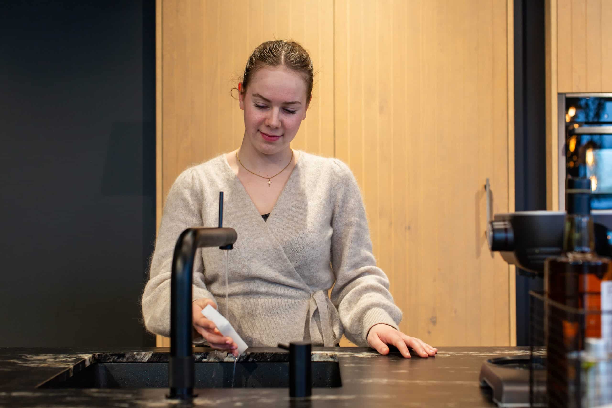 Gastvrouw Florine maakt de wonderspons nat ander de Quooker-kraan.